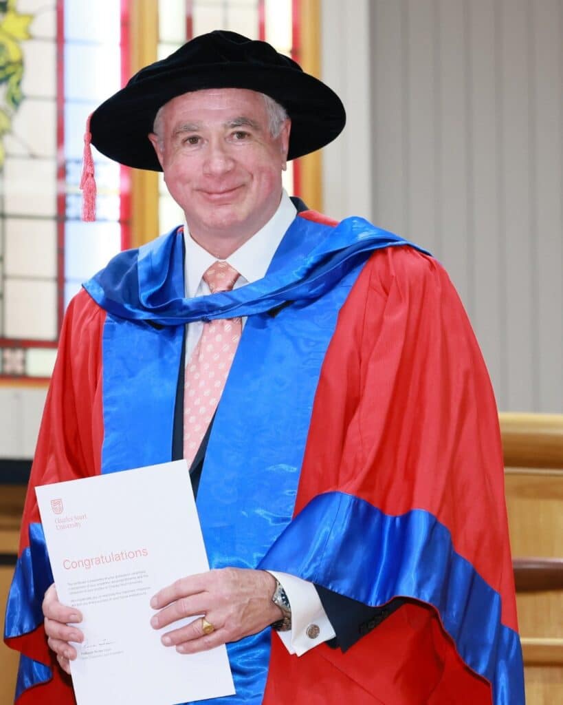 Dr John Goddard in doctoral robes at his Doctor of Business Administration graduation, Charles Sturt University, 2026